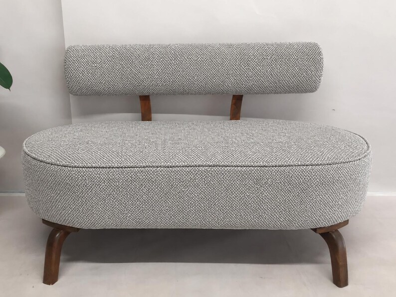 May include: A small loveseat featuring a rounded, oval-shaped seat upholstered in a textured grey and white woven fabric. It has a low, rectangular backrest supported by two wooden posts and stands on four curved, dark brown wooden legs.