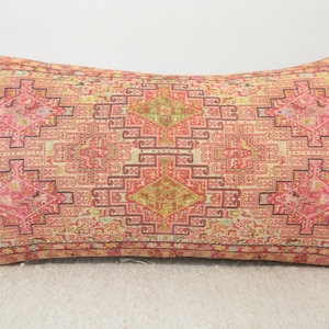 May include: A rectangular pillow with a pink, red, and cream patterned design. The pattern is a geometric design with a central diamond shape.