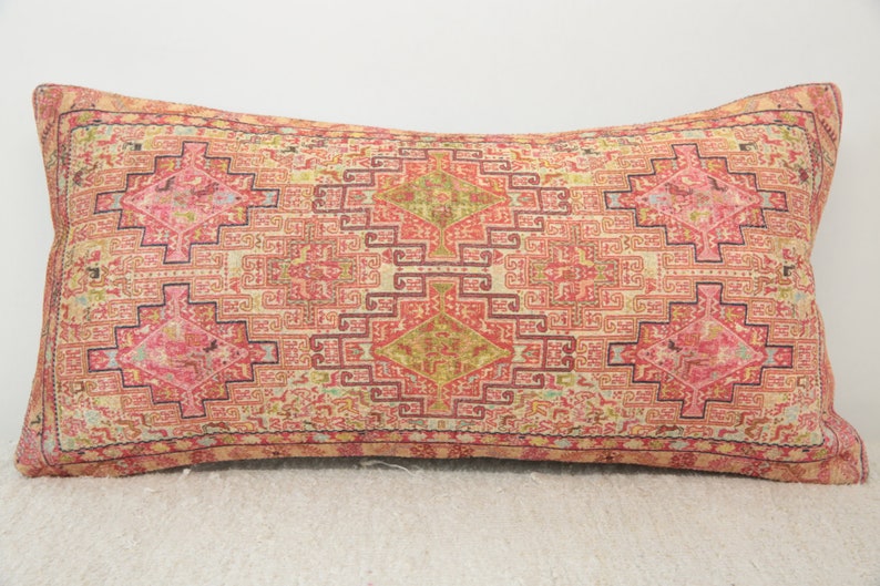 May include: A rectangular pillow with a pink, red, and cream patterned design. The pattern is a geometric design with a central diamond shape.