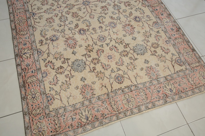 May include: A vintage rug with a cream background and a floral pattern in shades of pink, blue, and gray. The rug has a border with a repeating pattern of flowers and leaves.