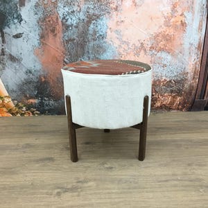 May include: A white fabric ottoman with a colorful patterned top and dark brown wooden legs.