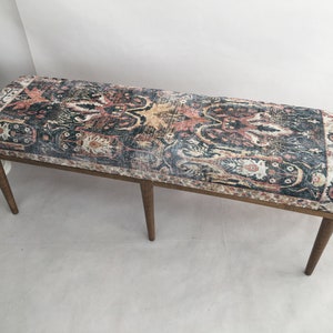 May include: A long wooden bench with four legs and a dark blue, red, and cream patterned fabric seat.