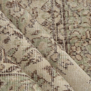 K&ouml;nnte beinhalten: Nahaufnahme eines beige-braunen gemusterten Teppichs mit einem dezenten Gr&uuml;nton. Der Teppich hat eine gewebte Textur und einen Fransenrand.