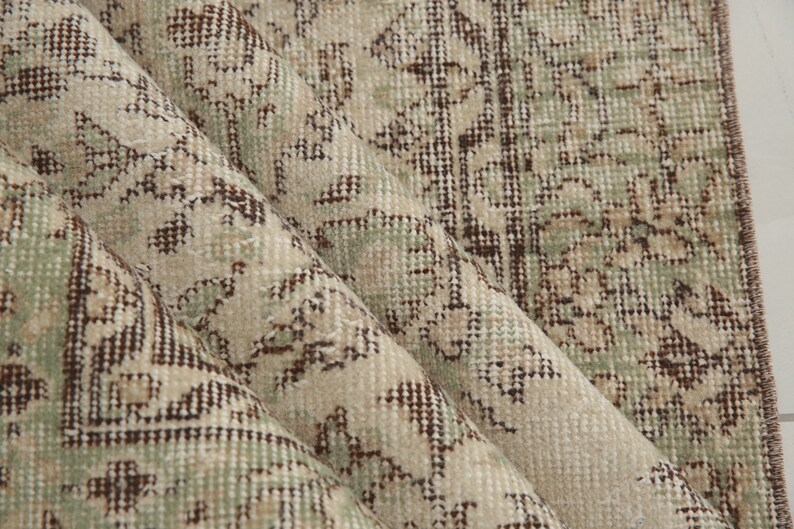 K&ouml;nnte beinhalten: Nahaufnahme eines beige-braunen gemusterten Teppichs mit einem dezenten Gr&uuml;nton. Der Teppich hat eine gewebte Textur und einen Fransenrand.