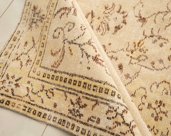 May include: A beige rug with a brown floral pattern. The rug is folded in half, showing the underside of the rug.