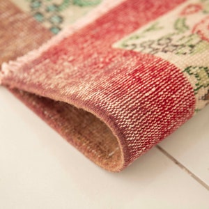 May include: Close-up of the edge of a red and white patterned rug with floral designs. The rug is woven with a textured, hand-knotted style.