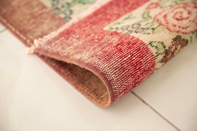 May include: Close-up of the edge of a red and white patterned rug with floral designs. The rug is woven with a textured, hand-knotted style.
