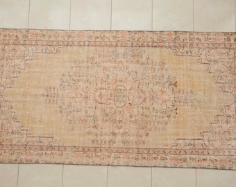 May include: A rectangular area rug featuring a central medallion and intricate floral patterns in shades of muted orange, beige, and dark gray. The design includes a detailed border with repeating geometric and botanical motifs throughout the piece.