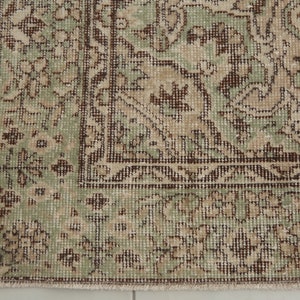 K&ouml;nnte beinhalten: Ein Vintage-Teppich mit einem gr&uuml;nen und braunen Blumenmuster. Der Teppich hat einen Fransenrand und ist aus einem weichen, gewebten Material.