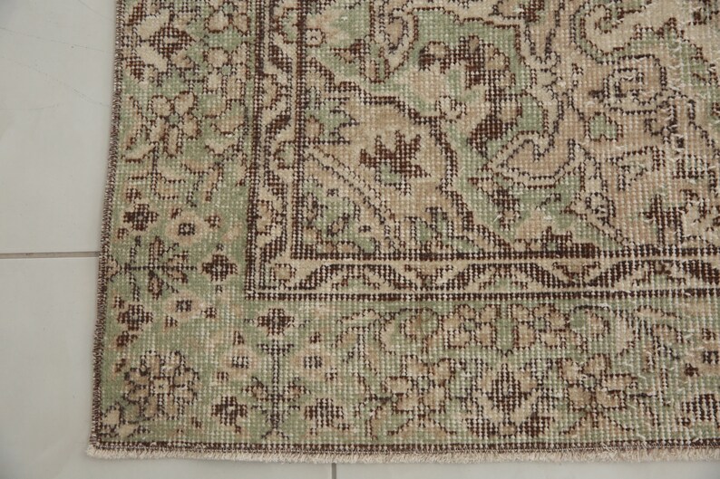 K&ouml;nnte beinhalten: Ein Vintage-Teppich mit einem gr&uuml;nen und braunen Blumenmuster. Der Teppich hat einen Fransenrand und ist aus einem weichen, gewebten Material.