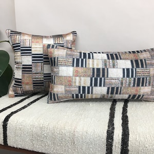 May include: Two decorative throw pillows with a black, white, and beige patchwork pattern. The pillows are on a white and black striped couch.