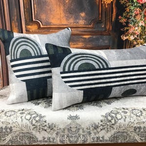 May include: Two decorative throw pillows with a geometric pattern in shades of gray, black, and green. The pillows are made of a soft, textured fabric.