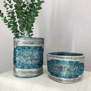 Pode incluir: Duas cestas de armazenamento de tecido com padrão azul turquesa e creme com uma planta verde de folhas na cesta mais alta.