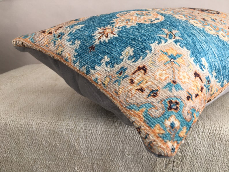 May include: A blue and beige patterned throw pillow with a fringe border. The pillow is made of a soft, woven fabric and has a subtle sheen.