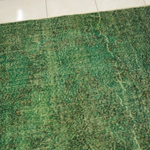 K&ouml;nnte beinhalten: Ein gr&uuml;ner Vintage-Teppich mit einem abgenutzten Look. Der Teppich hat ein dezentes Muster und eine verblichene Optik.