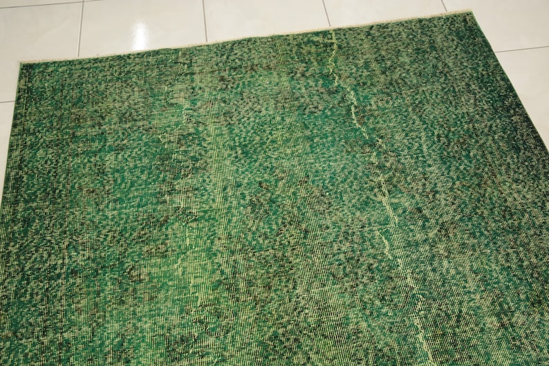 K&ouml;nnte beinhalten: Ein gr&uuml;ner Vintage-Teppich mit einem abgenutzten Look. Der Teppich hat ein dezentes Muster und eine verblichene Optik.