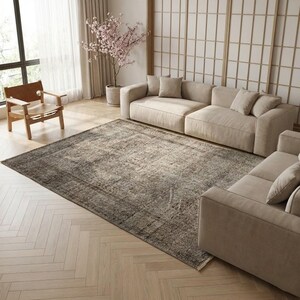 May include: A large rectangular area rug featuring a distressed, vintage-inspired pattern in shades of charcoal, grey, and beige. The rug has a low-pile texture and is positioned on a light-coloured herringbone wood floor in a living room setting.