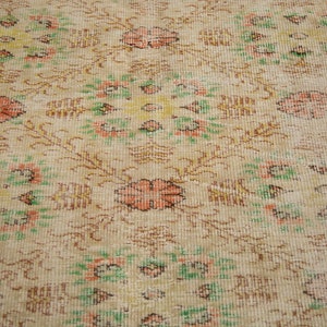 May include: A vintage rug with a floral pattern in shades of pink, green, and yellow. The rug has a faded, distressed look and a peach-colored border.