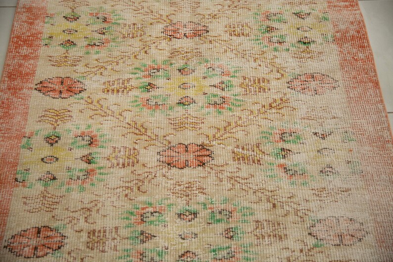 May include: A vintage rug with a floral pattern in shades of pink, green, and yellow. The rug has a faded, distressed look and a peach-colored border.