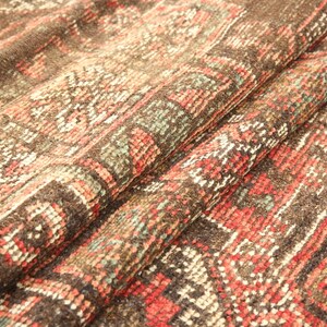 a close-up view of a colorful, intricately patterned fabric, possibly a rug or textile. The fabric has a vibrant mix of red, orange, and green colors, creating a visually striking and detailed design. The fabric appears to be folded or rolled, revealing its intricate patterns and textures.