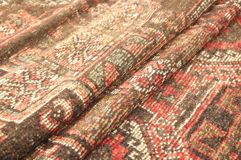 a close-up view of a colorful, intricately patterned fabric, possibly a rug or textile. The fabric has a vibrant mix of red, orange, and green colors, creating a visually striking and detailed design. The fabric appears to be folded or rolled, revealing its intricate patterns and textures.