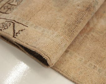 Può includere: Un tappeto beige a pelo corto con un angolo ripiegato. Il tappeto presenta un bordo geometrico marrone scuro con motivi floreali lungo il margine, che contrasta con il centro a tinta unita e di colore neutro del tessuto intrecciato.