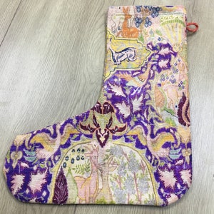 May include: A purple, pink, and yellow Christmas stocking with a floral and animal design. The stocking is made of a woven fabric and has a loop at the top.