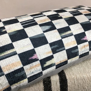 Puede incluir: Una almohada de tiro a cuadros en blanco y negro con un sutil patr&oacute;n ikat en tonos de rosa, azul y amarillo. La almohada tiene un borde gris y est&aacute; hecha de una tela suave y mullida.
