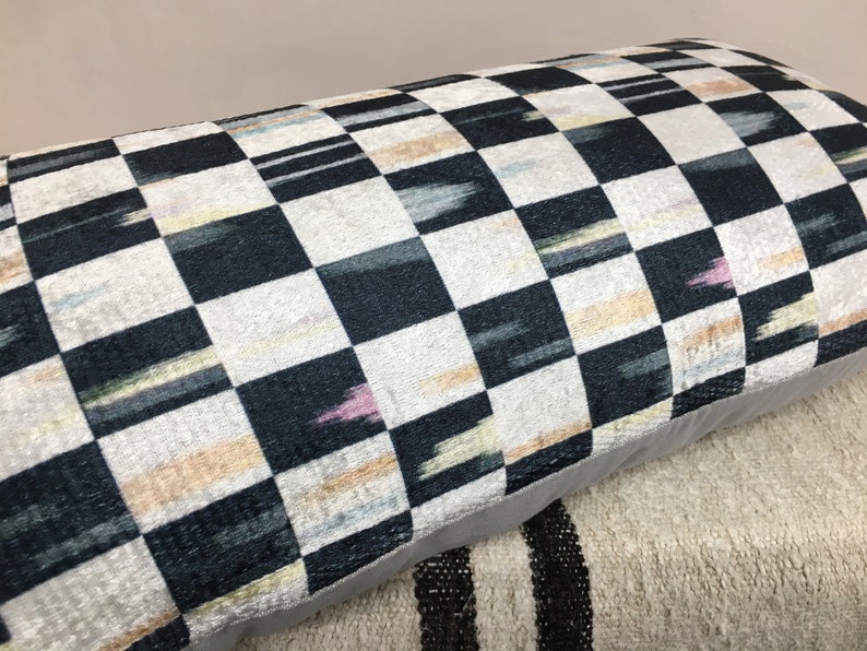 Puede incluir: Una almohada de tiro a cuadros en blanco y negro con un sutil patr&oacute;n ikat en tonos de rosa, azul y amarillo. La almohada tiene un borde gris y est&aacute; hecha de una tela suave y mullida.