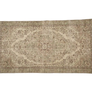 K&ouml;nnte beinhalten: Ein Vintage-Teppich mit beigefarbenem Hintergrund und einem floralen Muster in Braun- und Gr&uuml;nt&ouml;nen. Der Teppich hat einen Rand mit einem sich wiederholenden Muster.