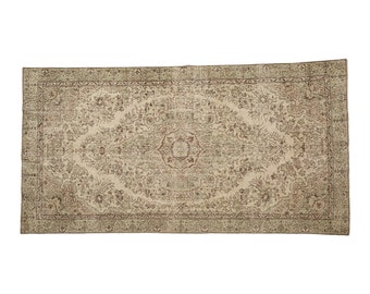 Könnte beinhalten: Ein Vintage-Teppich mit beigefarbenem Hintergrund und einem floralen Muster in Braun- und Grüntönen. Der Teppich hat einen Rand mit einem sich wiederholenden Muster.