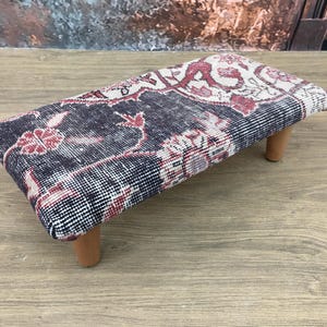 Peut inclure: Un repose-pieds rectangulaire avec un dessus à motifs bleu marine, rouge et crème. Le motif présente des motifs floraux. Il est soutenu par quatre pieds courts en bois brun clair. Style vintage ou antique.