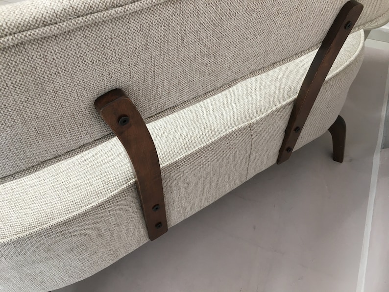 May include: A beige upholstered sofa featuring a textured fabric finish and curved dark brown wooden support legs attached to the backrest with visible black screws. The sofa has a structured frame with a clean, neutral-toned textile.