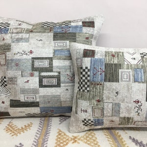 May include: Two decorative throw pillows with a geometric pattern in shades of gray, blue, and brown. The pillows are made of a soft, textured fabric and have a subtle sheen.