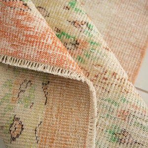 May include: Close-up of a beige and orange rug with a floral pattern. The rug has a fringed edge and is folded in half.