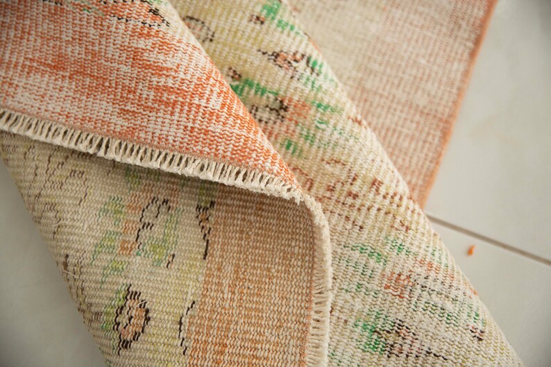 May include: Close-up of a beige and orange rug with a floral pattern. The rug has a fringed edge and is folded in half.