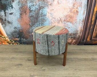 May include: A round, gray and beige patterned ottoman with wooden legs. The ottoman is sitting on a wood floor.