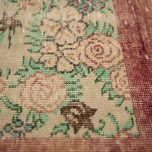 May include: Close-up of a beige rug with a floral pattern. The rug has a red border and is woven with a variety of colors, including green, pink, and blue.