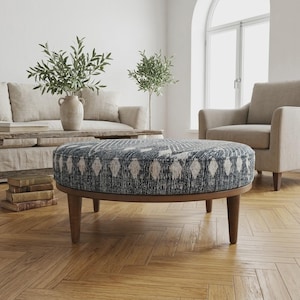 May include: A round ottoman featuring a dark blue and white patterned fabric upholstery with a geometric diamond design. The piece is supported by four tapered wooden legs in a medium brown finish, providing a stable base for this furniture item.