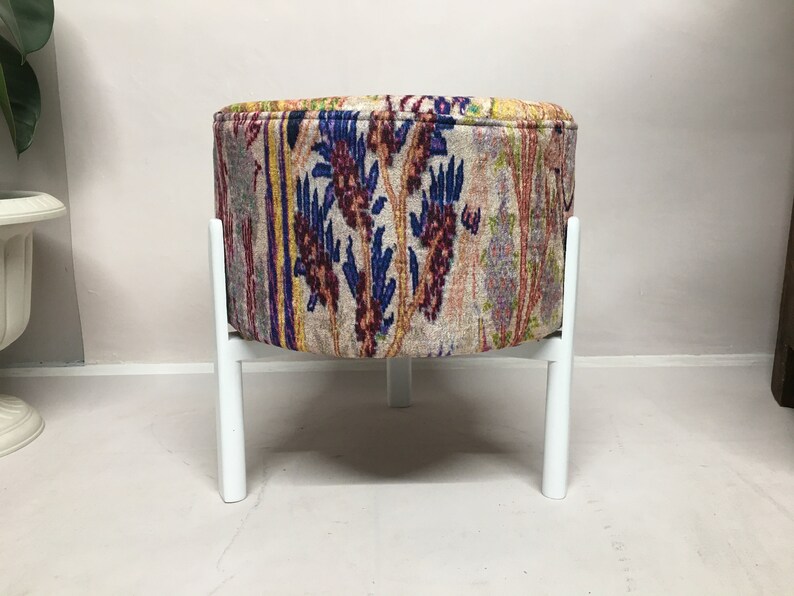 May include: A round, white-legged ottoman with a colorful floral patterned fabric cover.