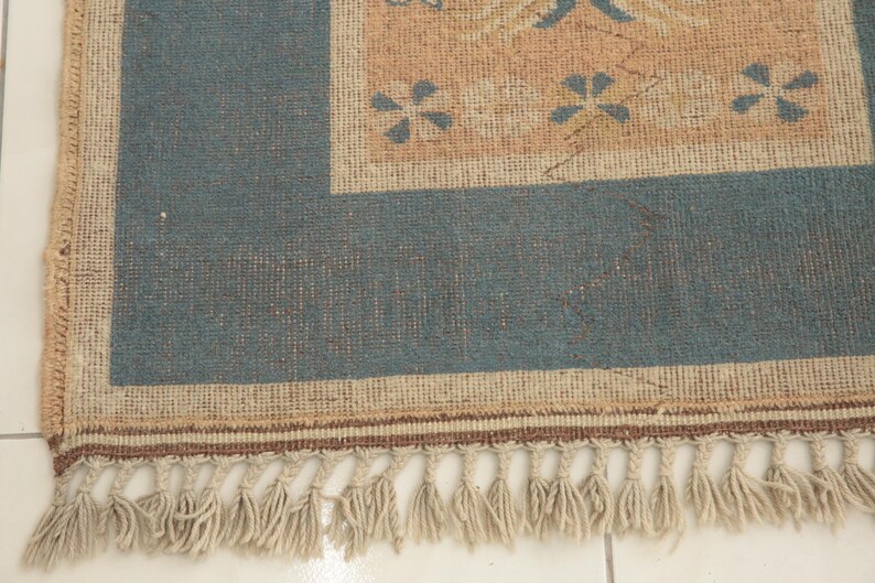 K&ouml;nnte beinhalten: Ein blauer und beiger Teppich mit Fransenrand. Der Teppich hat ein florales Muster in der Mitte.
