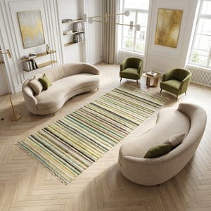 May include: A rectangular area rug featuring a multi-colored striped pattern in shades of green, brown, yellow, and cream. The rug has a textured surface with visible fringe detailing at both ends, positioned centrally on a light wood herringbone floor.