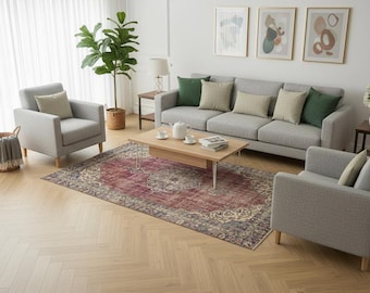 May include: A living room set featuring a light grey sofa and two matching armchairs with light wood legs. A rectangular wooden coffee table sits on a large, distressed red and blue patterned area rug. Green and beige throw pillows accent the seating.