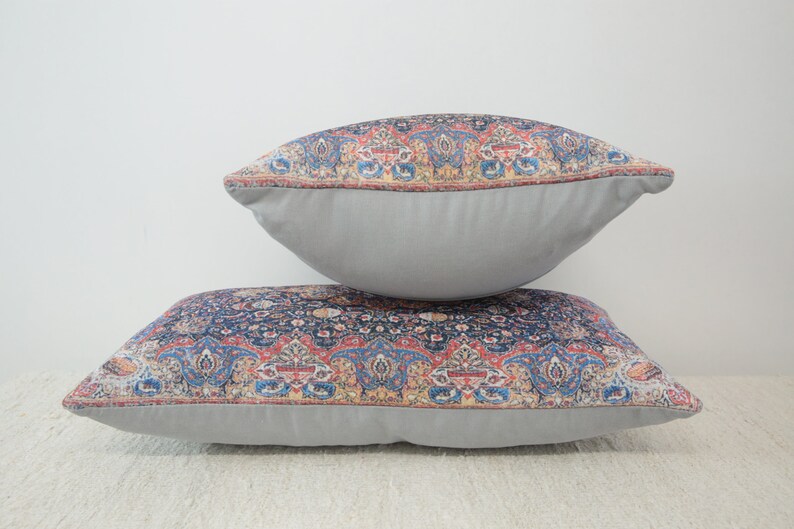 May include: Two decorative throw pillows with a gray fabric backing and a colorful patterned front. The pattern features a paisley design in shades of blue, red, and gold.