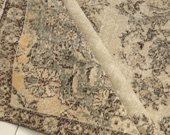 Könnte beinhalten: Ein beige-brauner Vintage-Teppich mit floralem Muster. Der Teppich hat einen Fransenrand und ist in der Mitte gefaltet.