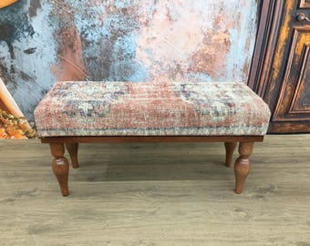 Puede incluir: Un banco de madera con patas torneadas tapizado en una tela estampada de colores. La tela tiene un aspecto vintage con tonos rojos, azules y crema.