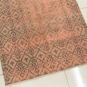 May include: A vintage rug with a geometric pattern in shades of pink, brown, and green. The rug has a fringed edge.