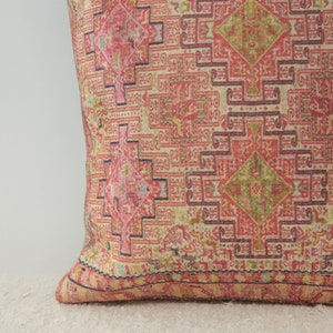 May include: A pink and cream throw pillow with a geometric pattern. The pillow has a dark blue border and a fringe around the edges.