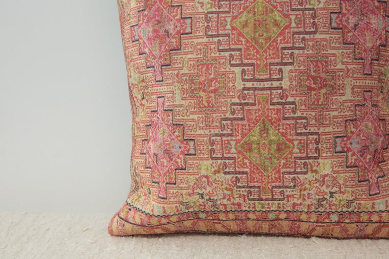 May include: A pink and cream throw pillow with a geometric pattern. The pillow has a dark blue border and a fringe around the edges.