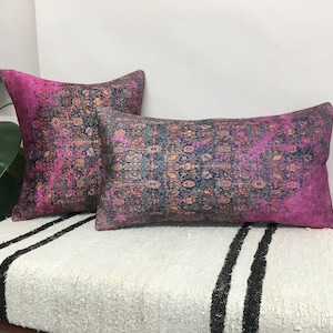 May include: Two decorative throw pillows with a pink and blue patterned design. The pillows are on a white and black striped surface.